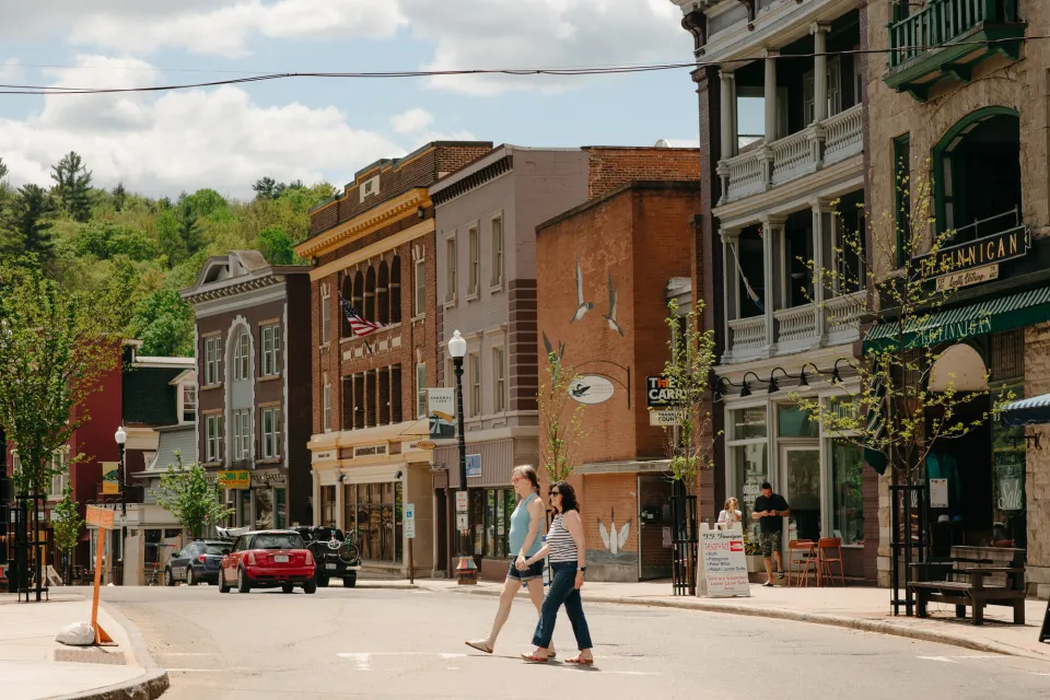 Two people walking across a street in downtown Saranac Lake.