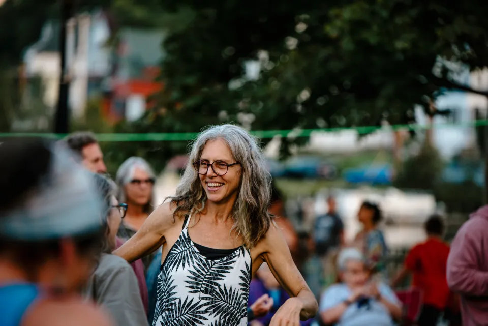 A woman with long gray hair dances at an outdoor summer music event.