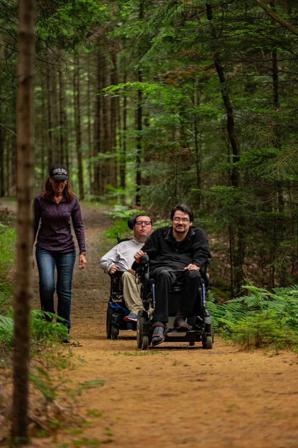 Two men in motorized wheelchairs ride on a wilderness trail.