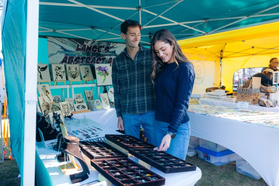 A man and woman look at handmade jewelry at a farmers market. 