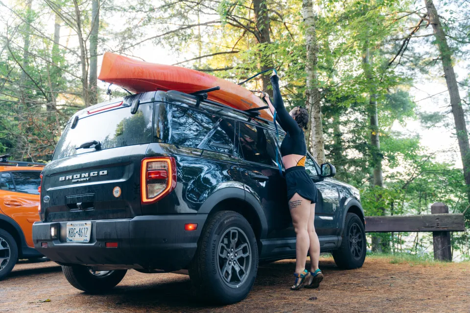 A woman takes a kayak off the roof of a car. 